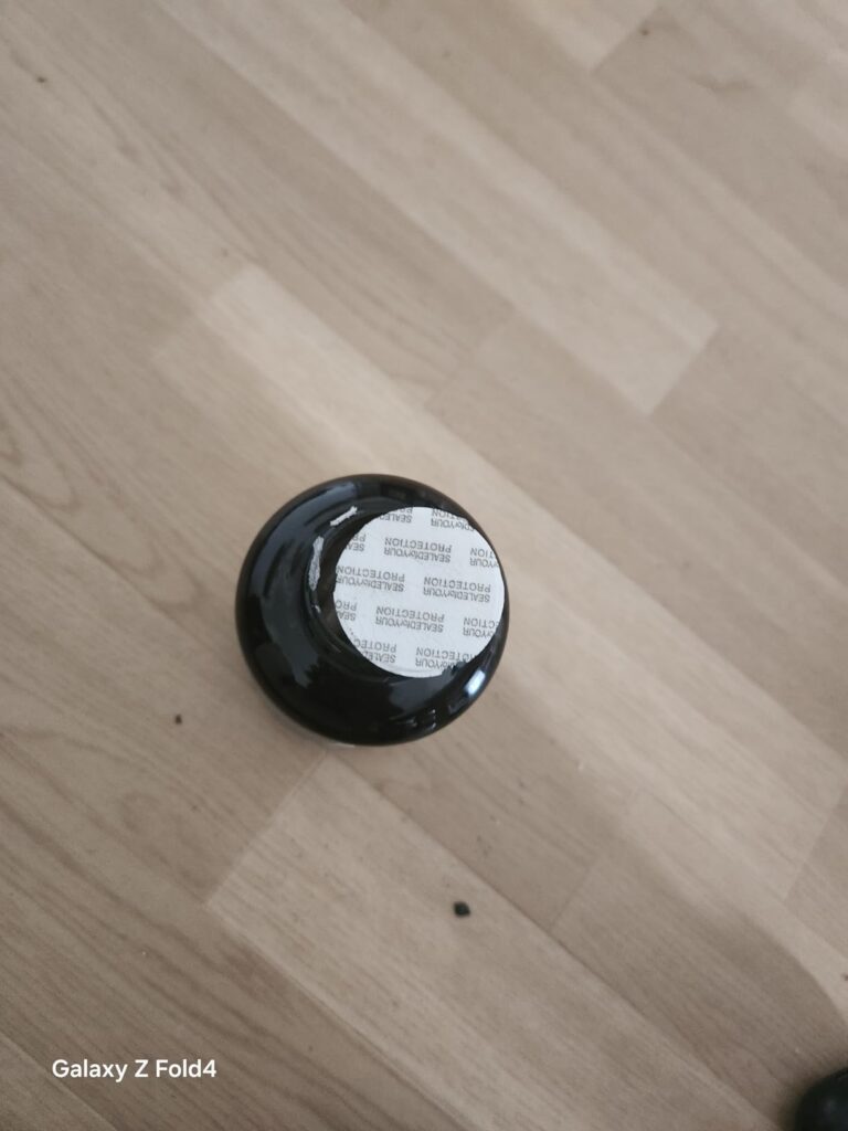 Photo du bouchon de la bouteille posé sur un parquet. Le bouchon est noir avec un opercule blanc à l'intérieur.