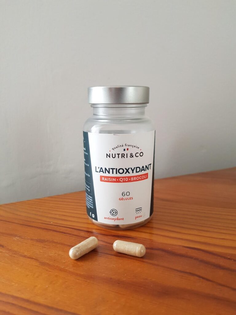 Flacon de Nutri & Co L'Antioxydant sur une table en bois, avec deux gélules en avant-plan. Le visuel 0 montre le même flacon...