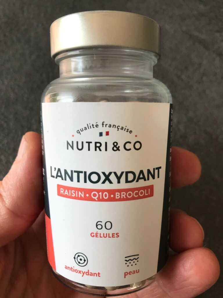 Flacon de Nutri & Co L'Antioxydant, tenue en main, de face. Le visuel 1 montre le même flacon sous un angle légèrement différ...