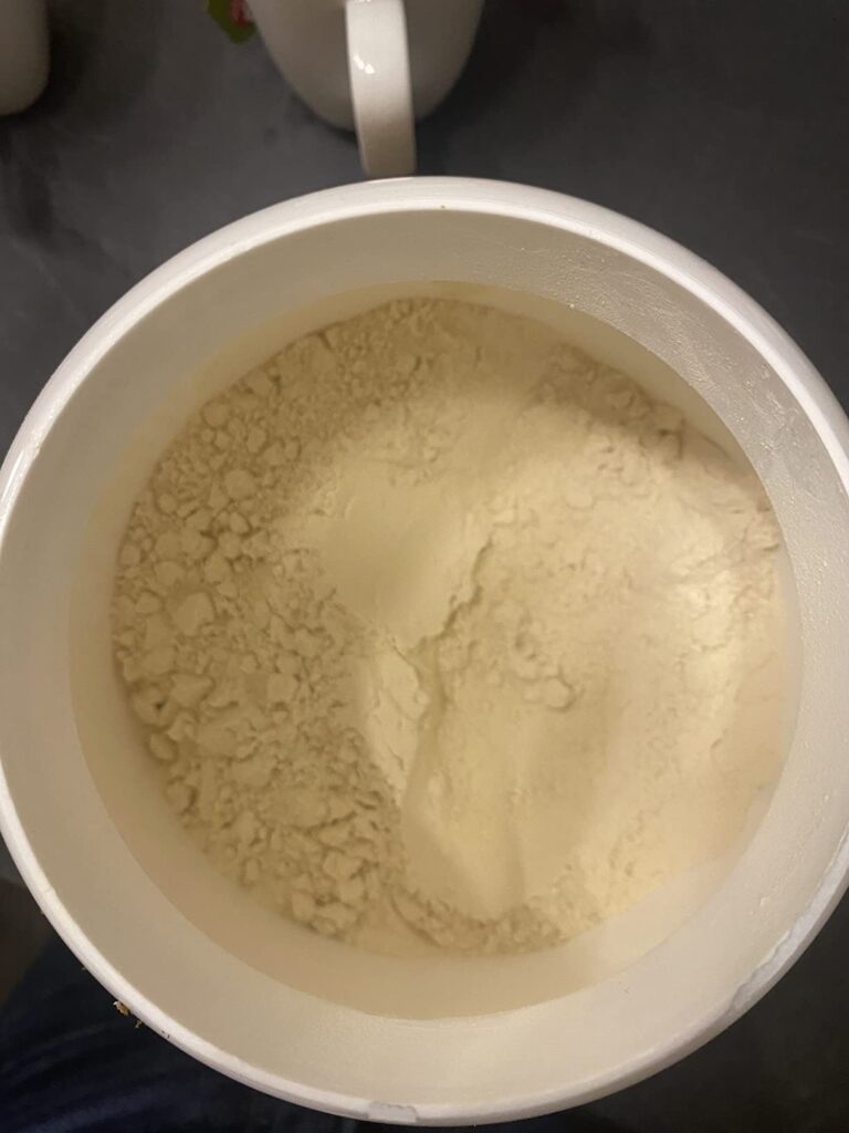 Un gros plan sur l'intérieur d'un pot de poudre de protéine. On peut voir la poudre de couleur blanc cassé.