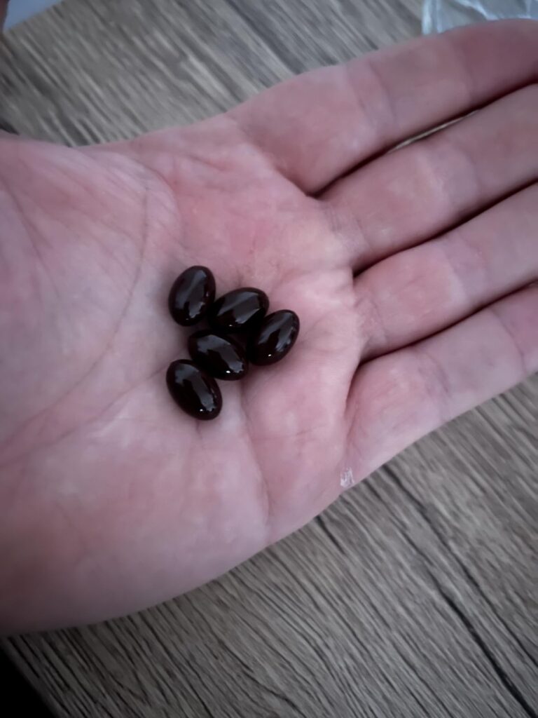 Six gélules de couleur sombre dans la paume d'une main.
