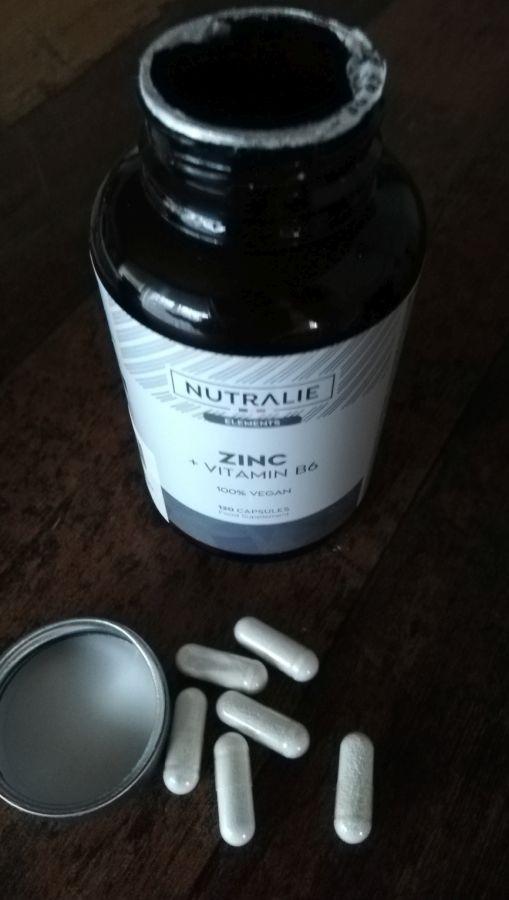Bouteille de zinc ouverte avec des capsules dispersées, vue de dessus. Le texte de l'étiquette est bien visible.