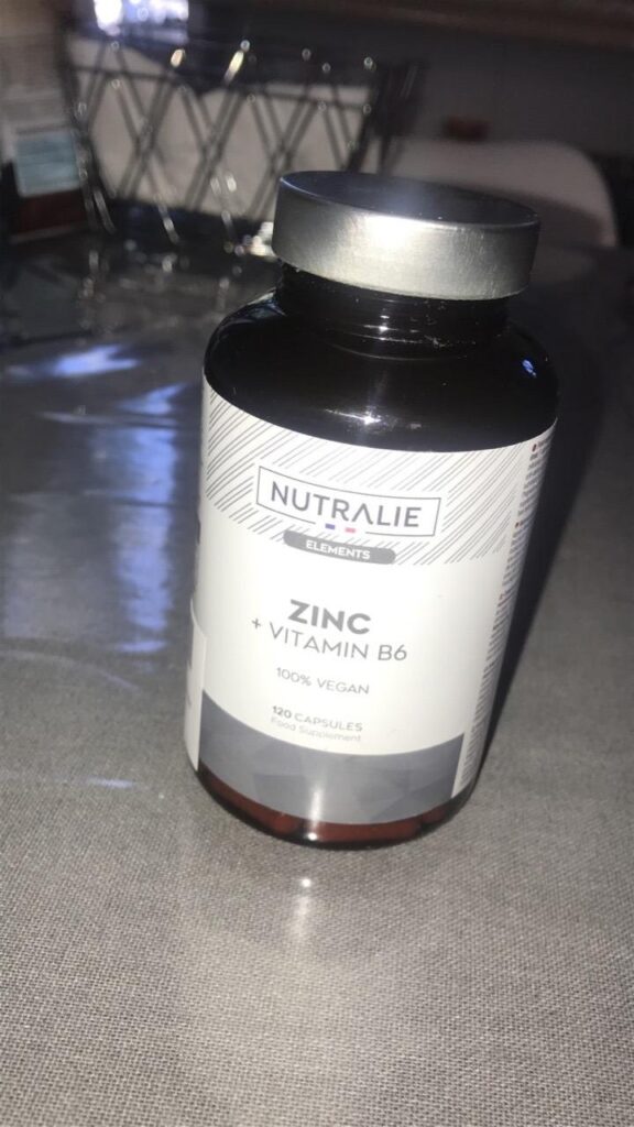 Bouteille de zinc fermée posée sur une table, légèrement de côté, montrant l'avant de l'étiquette. On aperçoit un panier en a...