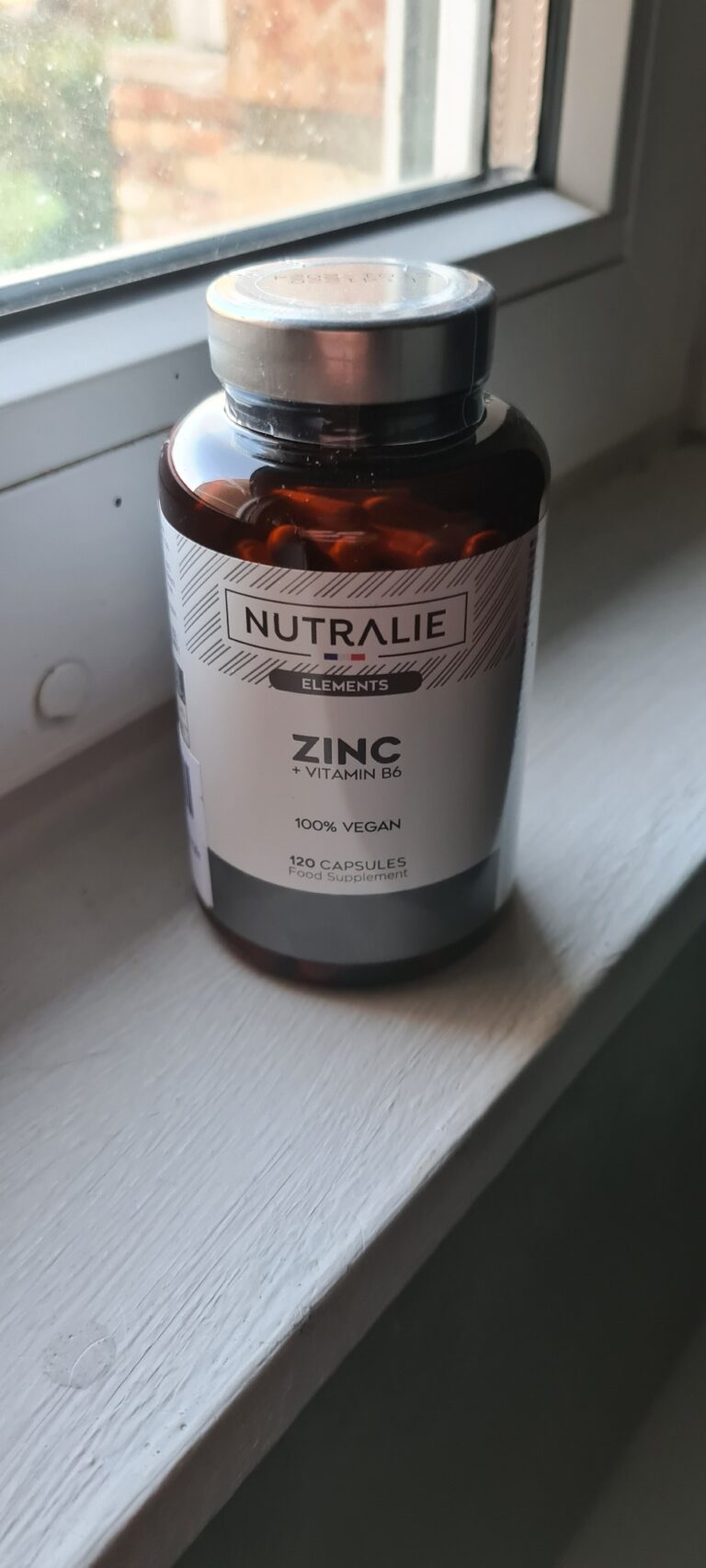 Bouteille de zinc fermée posée sur le rebord d'une fenêtre, montrant l'avant de l'étiquette. Vue légèrement de côté.