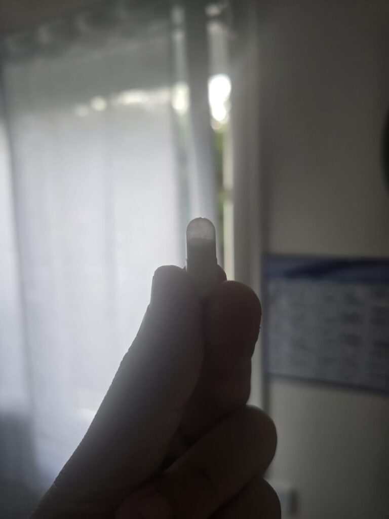 Gélule de citrate de magnésium tenue entre deux doigts, avec une fenêtre en arrière-plan.