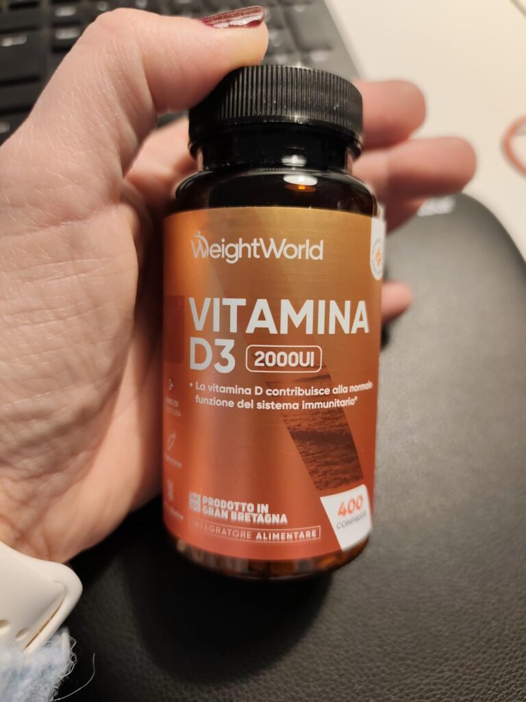 Une main tient le flacon de vitamine D3, vue légèrement de côté, montrant le produit en contexte.
