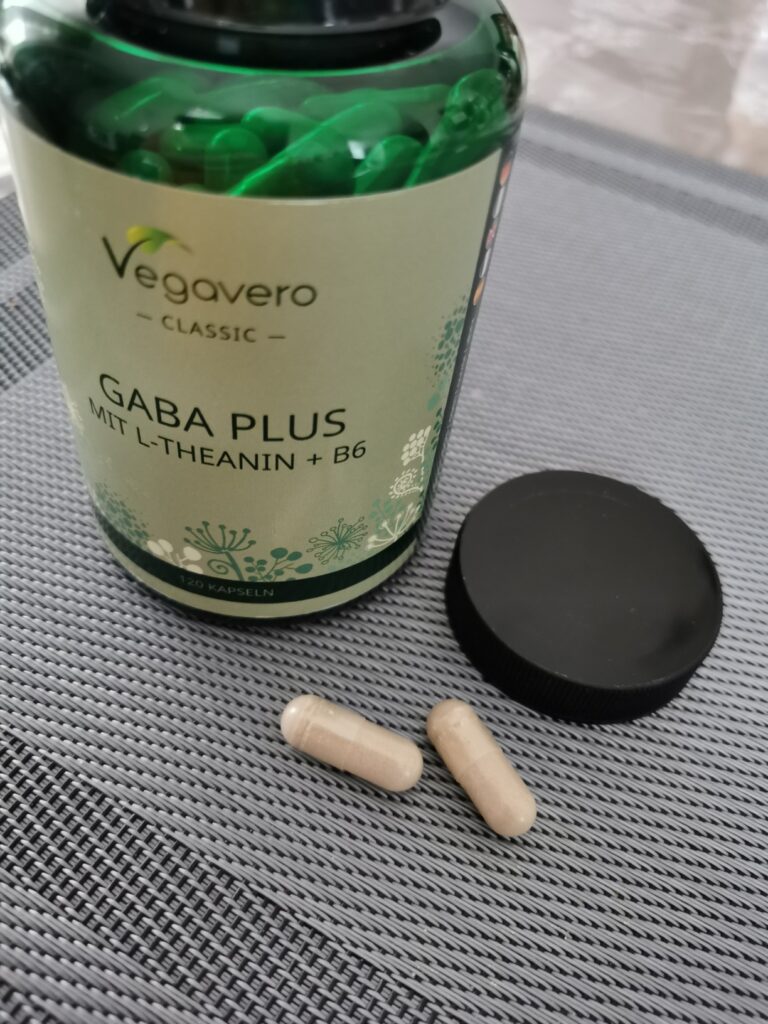 Le pot de complément alimentaire avec deux gélules et le couvercle à côté, sur un fond texturé. C'est le même produit que le...