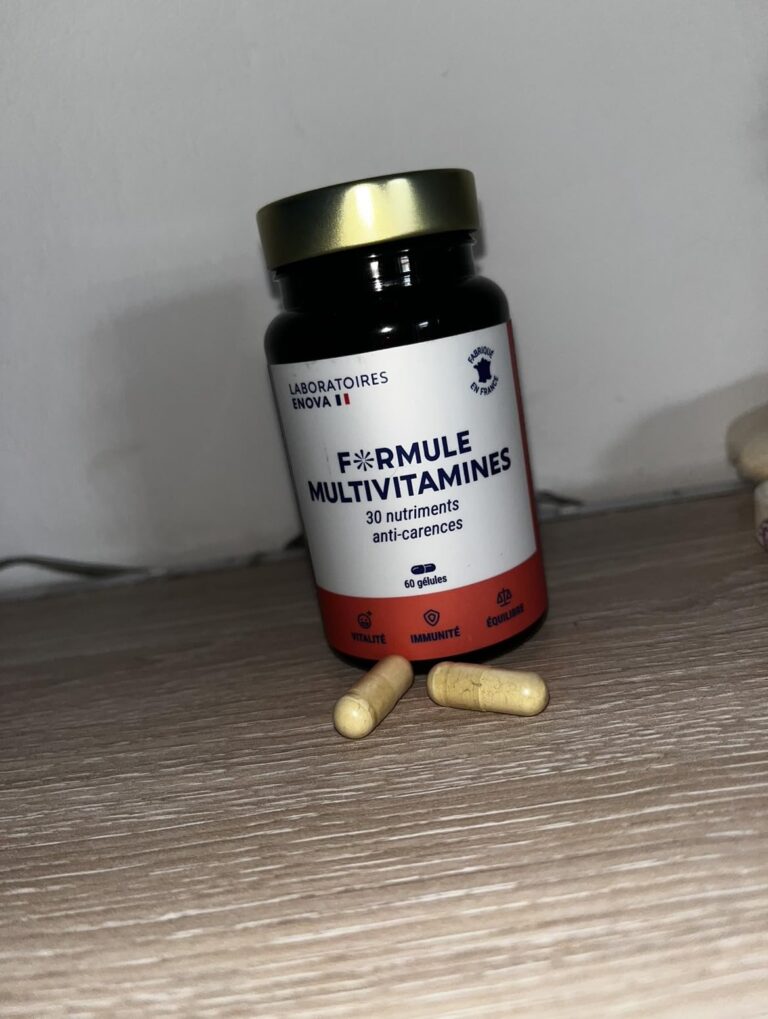 Le flacon de multivitamines et deux gélules posés sur un meuble en bois.