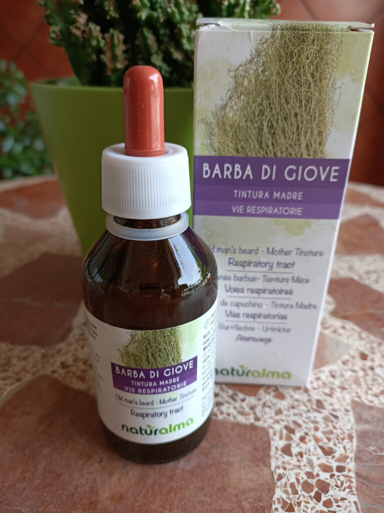 Bouteille de teinture mère avec pipette et sa boîte, posées sur une table avec une plante en arrière-plan.