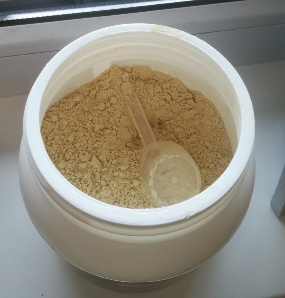 Vue de dessus du pot de complément alimentaire ouvert, montrant la poudre et la dosette.