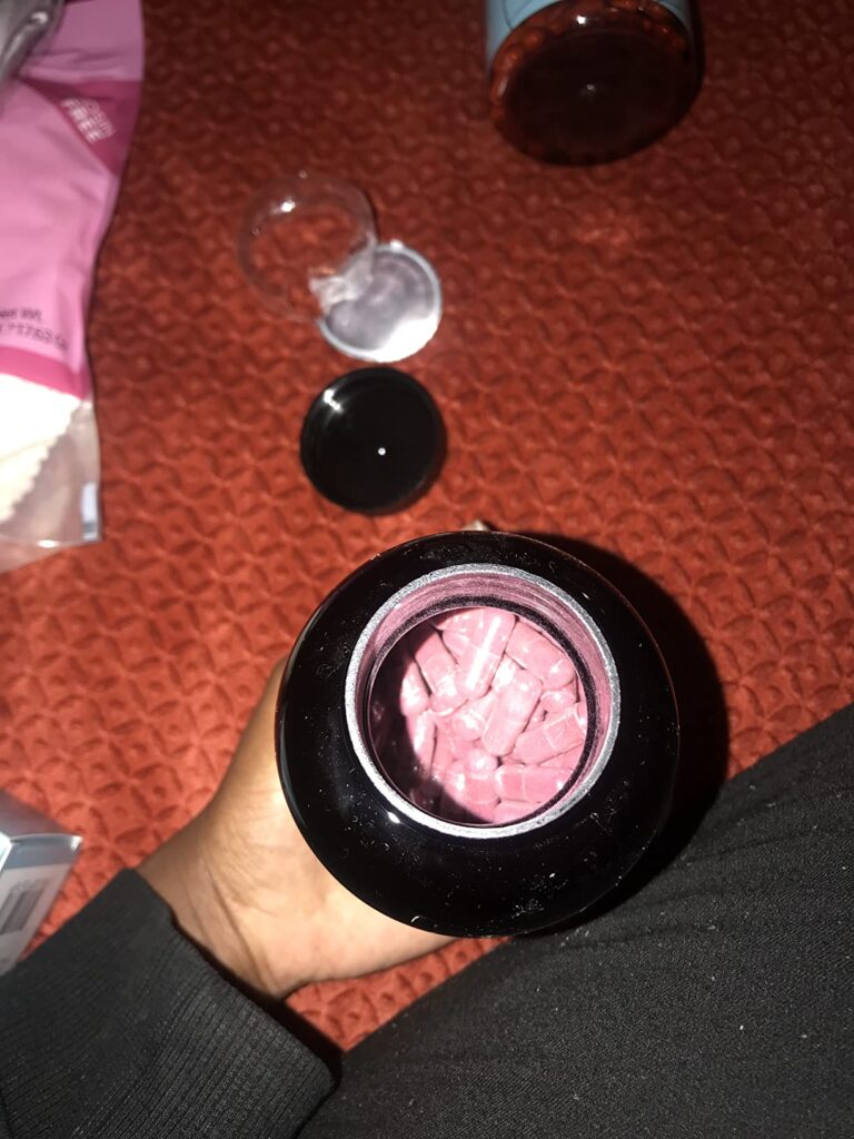 Gros plan sur le flacon ouvert, vue plongeante sur les gélules roses.