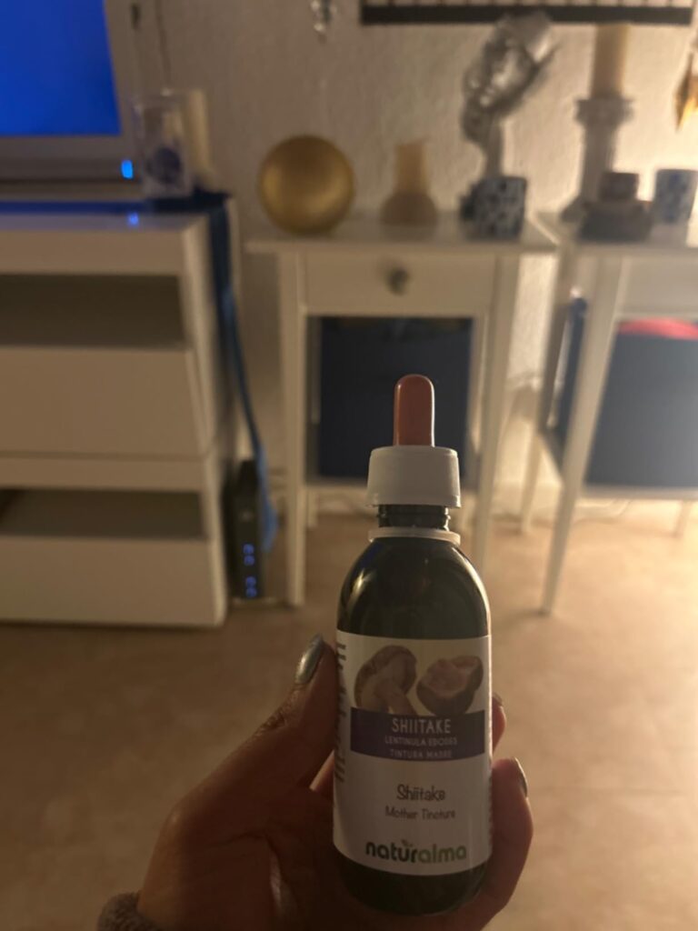 Une personne tient un flacon de teinture mère Shiitake dans la main, dans un salon éclairé à la lumière artificielle.