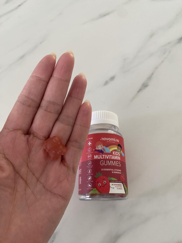 Main tenant une multivitamine gommeuse, avec la bouteille en arrière-plan sur un plan de travail en marbre.
