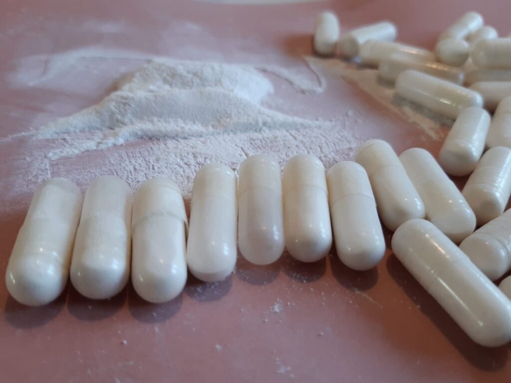 Gélules de NAC WeightWorld et poudre blanche sur fond rose.