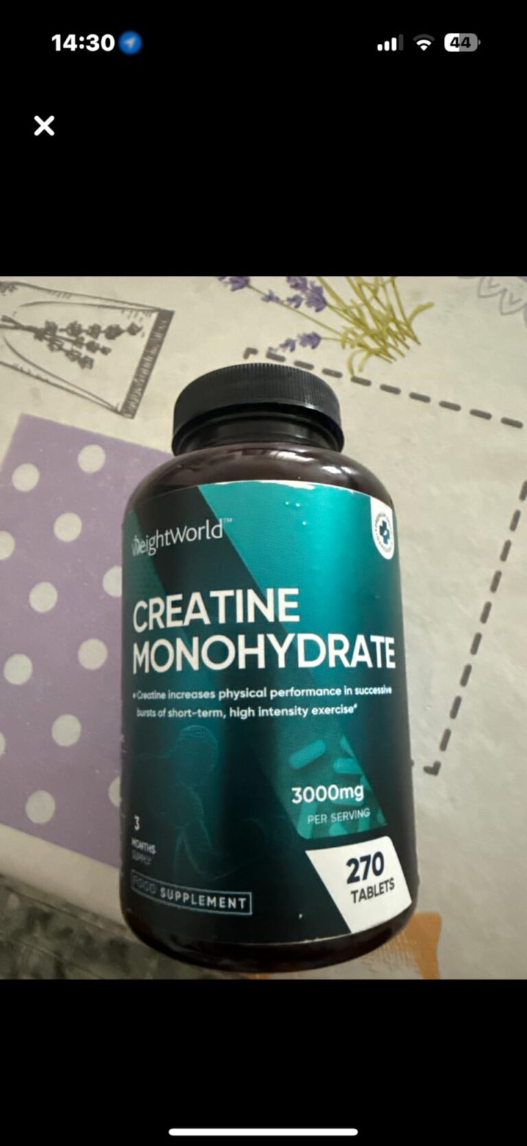 Bouteille de créatine monohydrate posée sur une table, prise depuis un téléphone.
