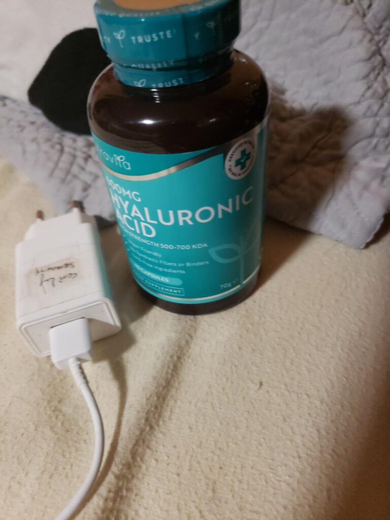 Bouteille de compléments alimentaires sur une table, avec un chargeur de téléphone à côté.