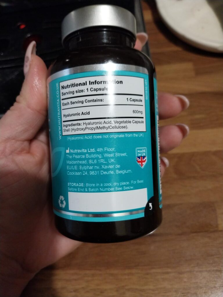 Bouteille de compléments alimentaires tenue dans une main, vue de dos montrant l'étiquette nutritionnelle.