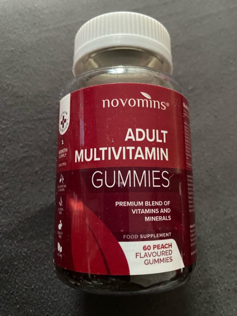 Un flacon de "Adult Multivitamin Gummies" de la marque Novomins, posé sur une surface sombre, l'étiquette principale face à l...