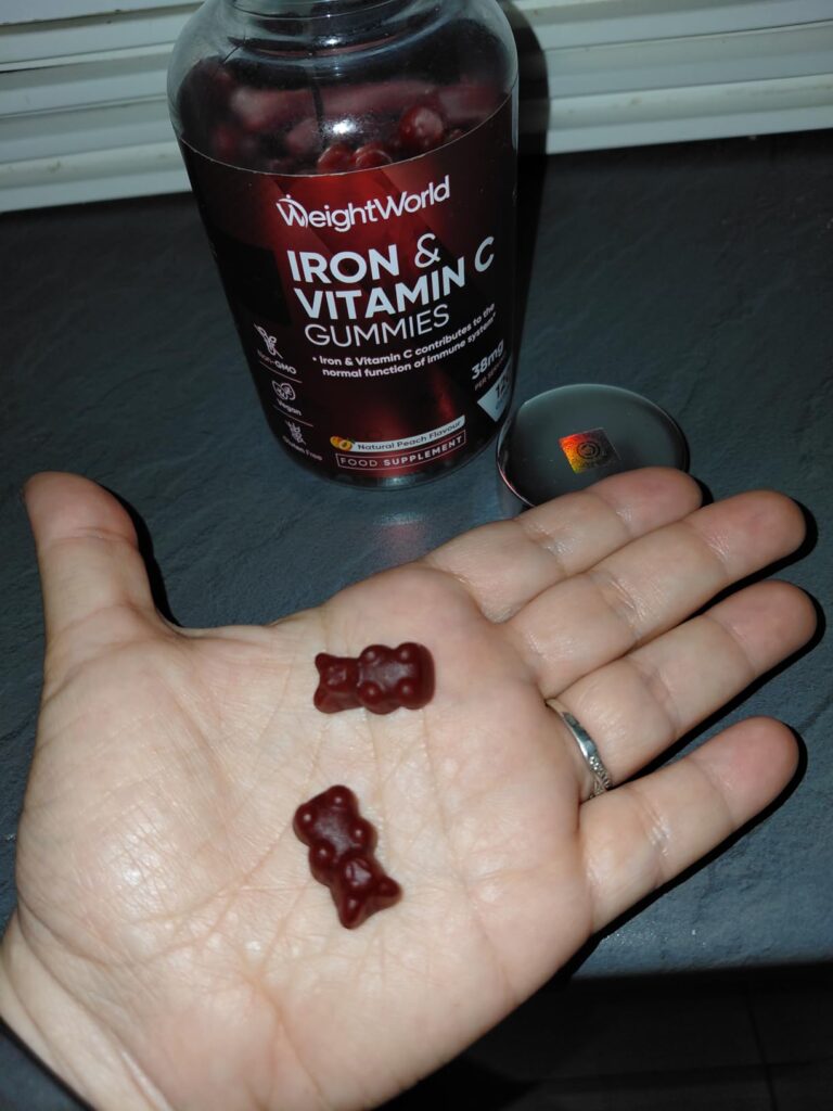 Deux oursons gélifiés dans la main d'une personne, avec le flacon de WeightWorld Iron & Vitamin C Gummies en arrière-plan.