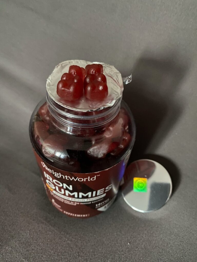 Le flacon de WeightWorld Iron Gummies est ouvert, le couvercle est à côté. On voit l'opercule de sécurité et les oursons géli...