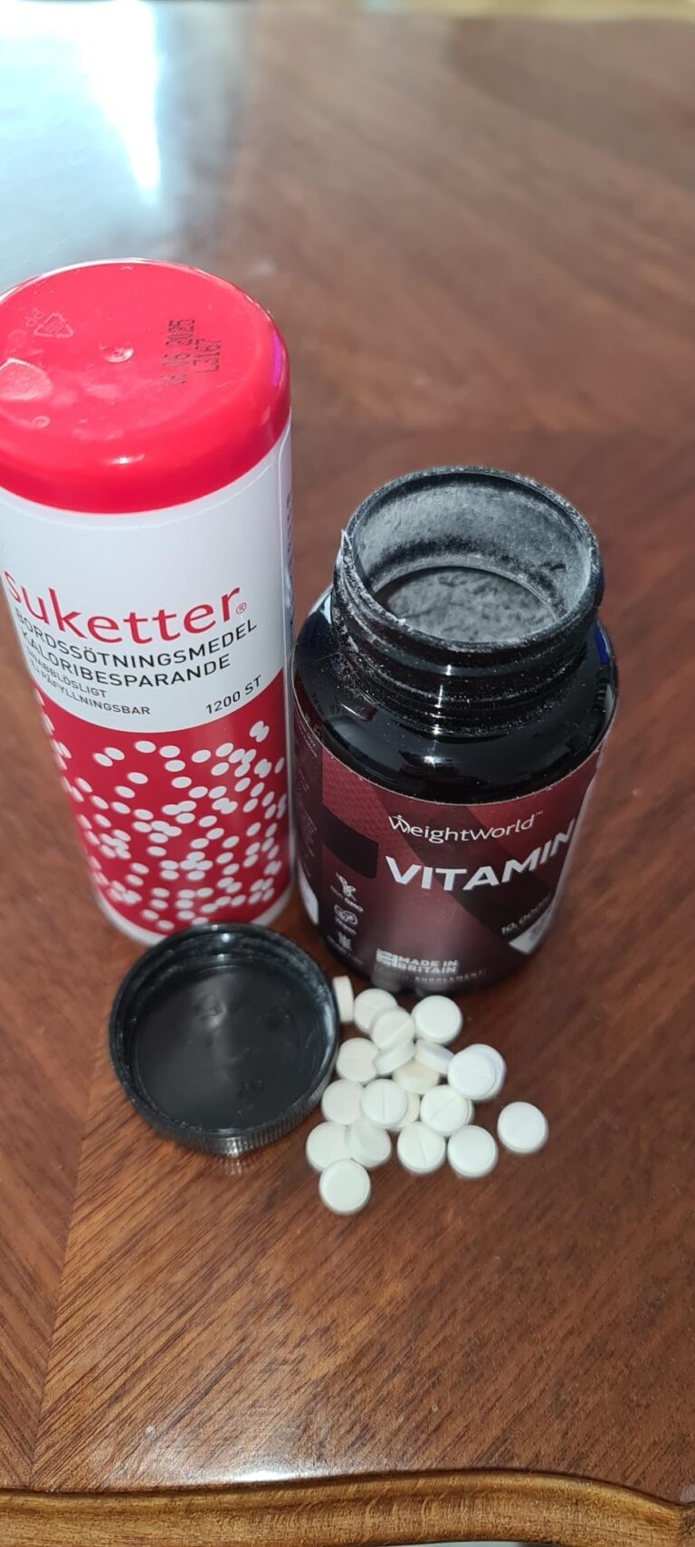 Le flacon de vitamine A est ouvert, avec des comprimés blancs étalés à côté. Un autre flacon blanc et rouge est posé à côté.