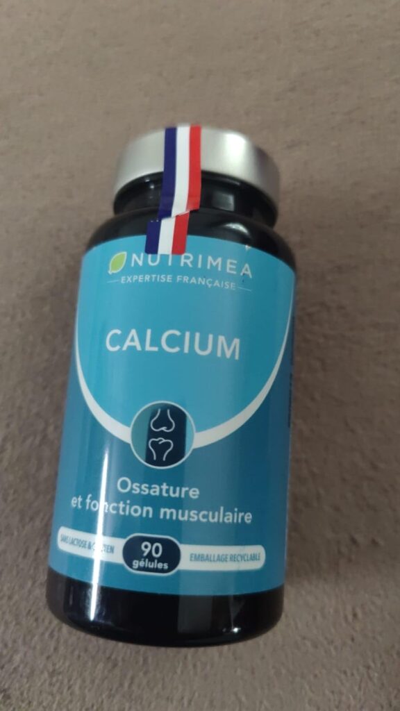 Un flacon de compléments alimentaires au calcium, en gros plan, posé sur un fond gris. Un ruban tricolore est collé sur le co...