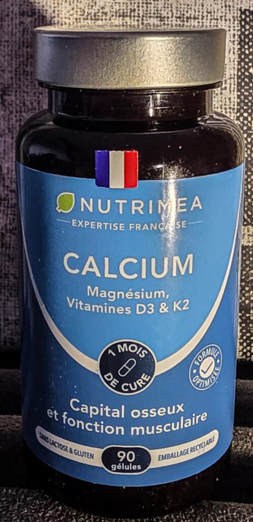 Un flacon de compléments alimentaires au calcium, en gros plan, posé sur un fond sombre. Un ruban tricolore est collé sur le...