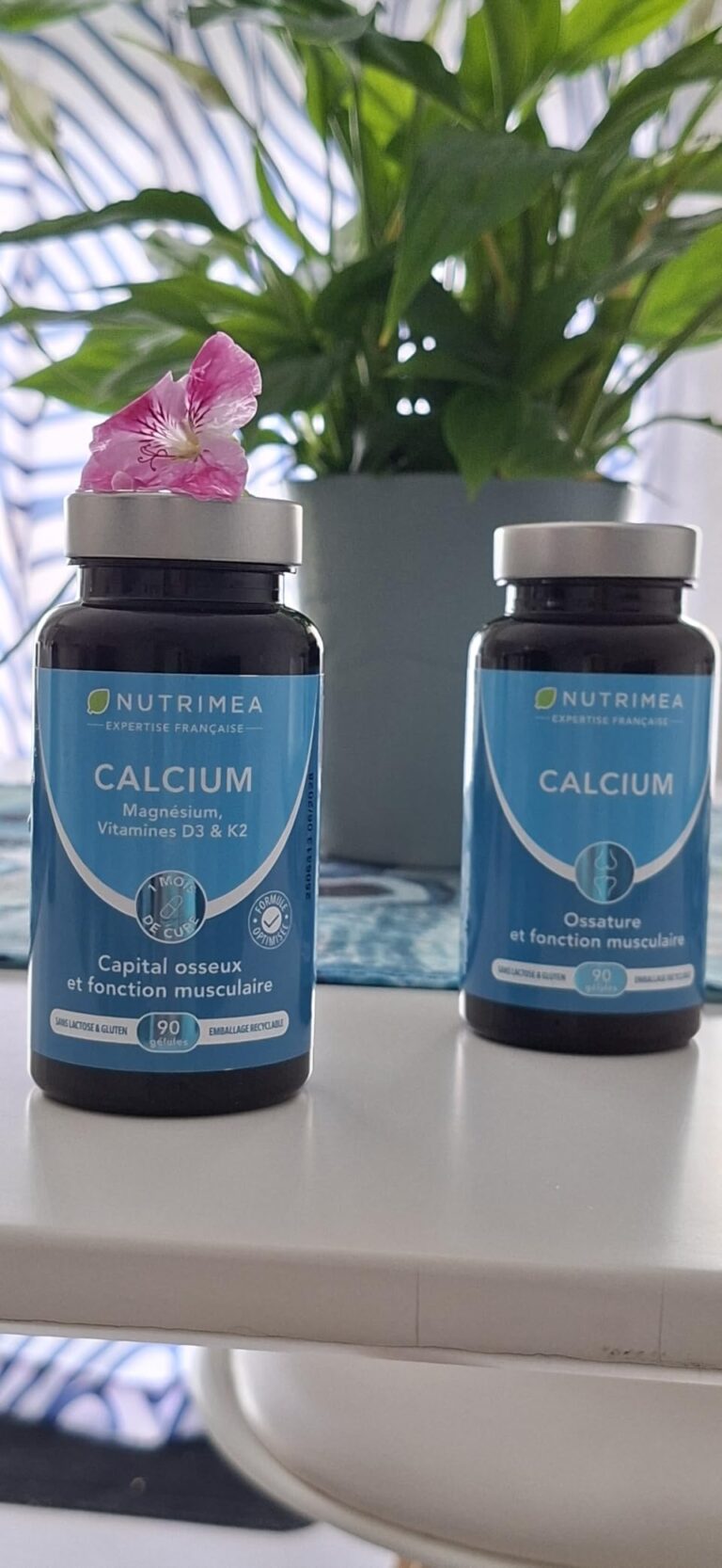 Deux flacons de compléments alimentaires au calcium posés sur une table blanche, avec une plante verte en arrière-plan. Une p...