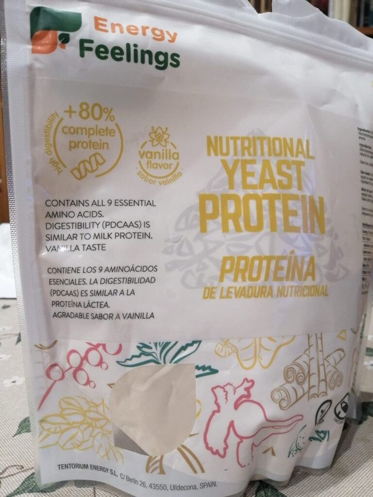 Vue de face du sachet de protéines sur un fond clair et fleuri. Le sachet est blanc avec un logo Energy Feelings en haut à ga...