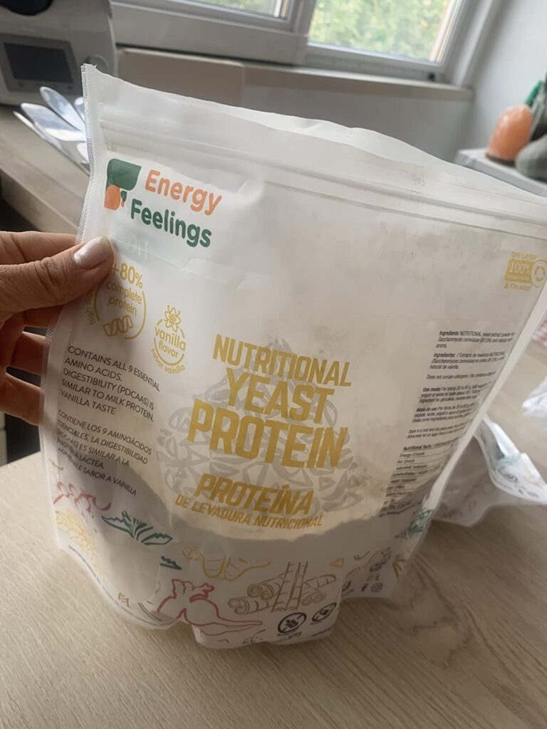 Une main tient le sachet de protéines. L'image est prise sous un angle similaire au visuel 0, mais en situation, dans une cui...