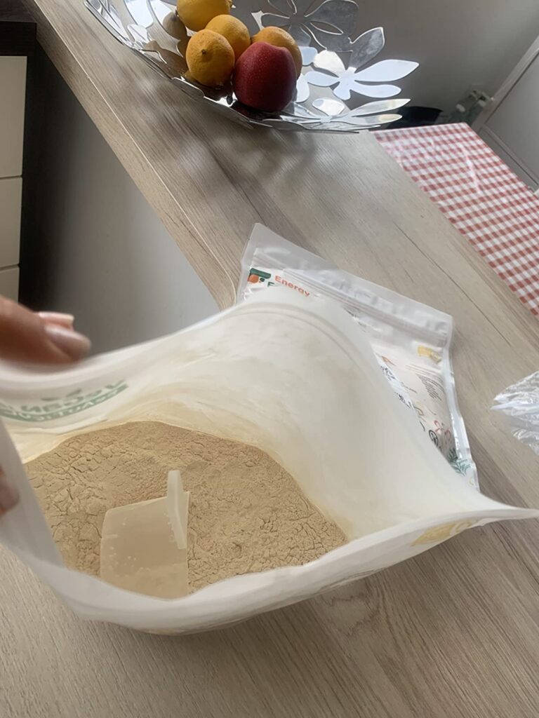 Vue intérieure du sachet de protéines, montrant la poudre et une cuillère doseuse. L'image est prise en situation, dans une c...