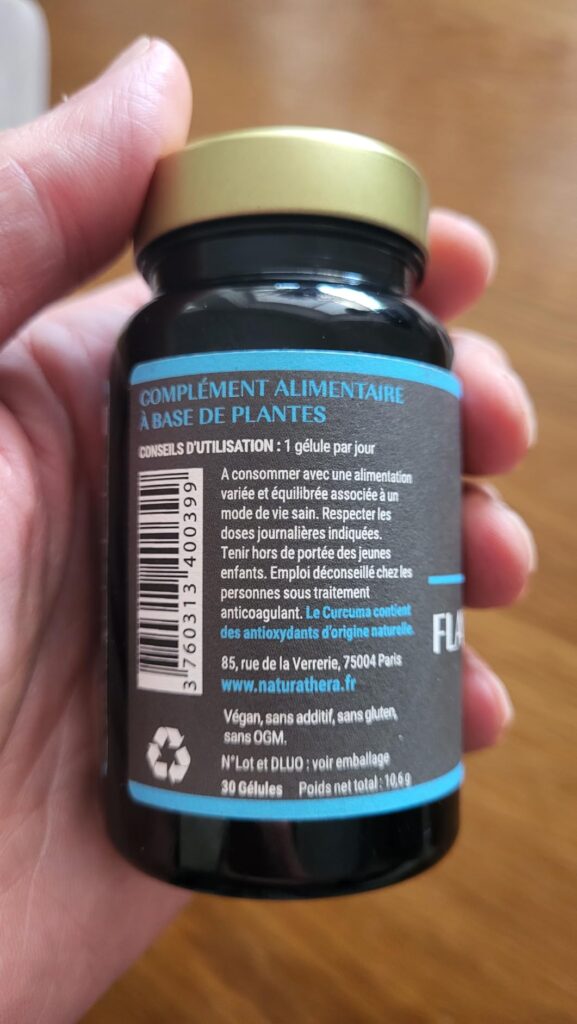 Flacon de compléments alimentaires tenu dans la main, face arrière visible, avec les informations légales et les conseils d'u...