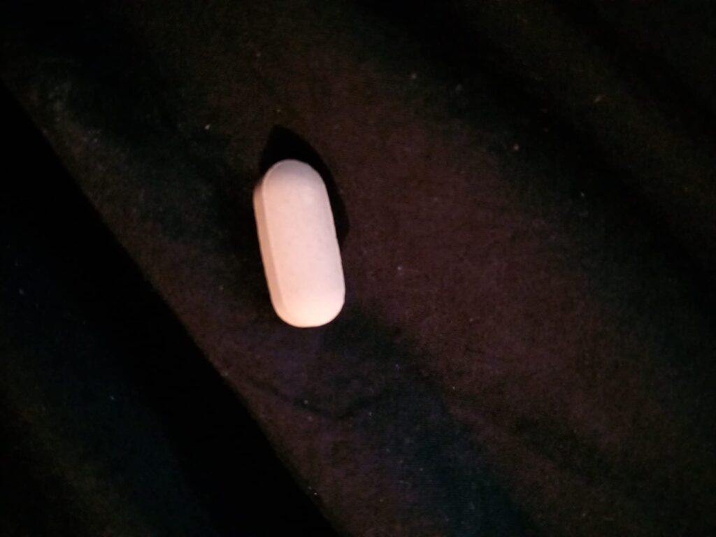 Une pilule blanche, de forme ovale, posée sur un tissu sombre.