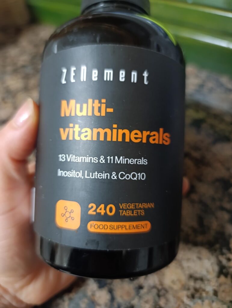 Flacon de compléments alimentaires 'ZENement Multivitaminerals', tenu par une main, vue de face, montrant la même étiquette q...