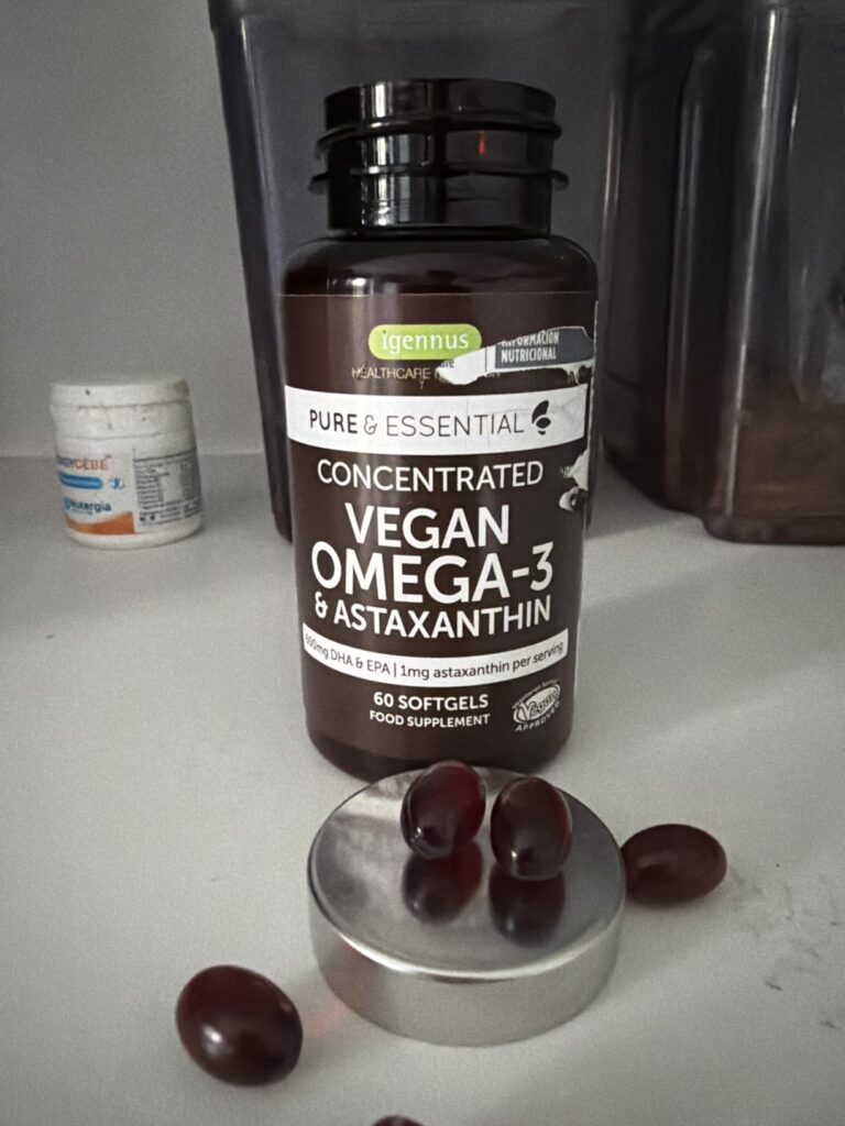 Flacon de gélules OMEGA-3 avec plusieurs gélules sorties, posées sur le couvercle et la surface. Les étiquettes du flacon son...