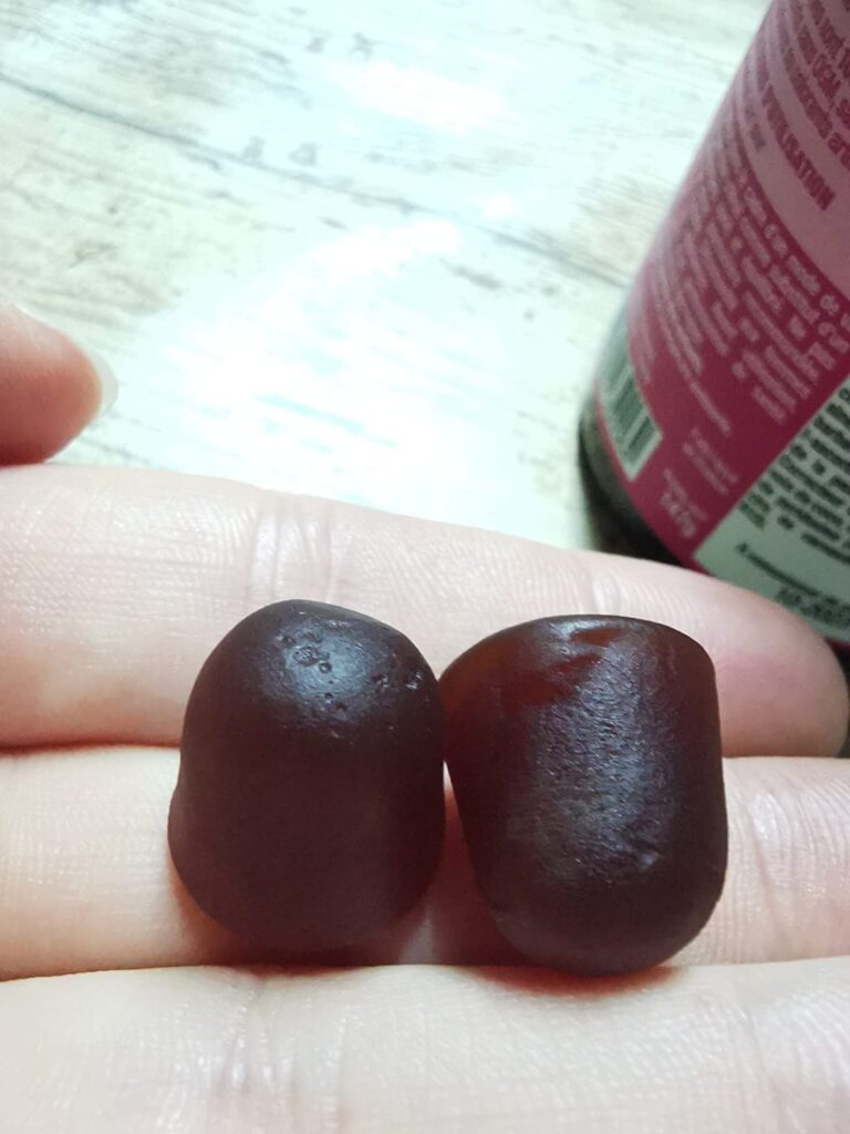 Deux bonbons tenus dans une main, avec une partie du flacon en arrière-plan.