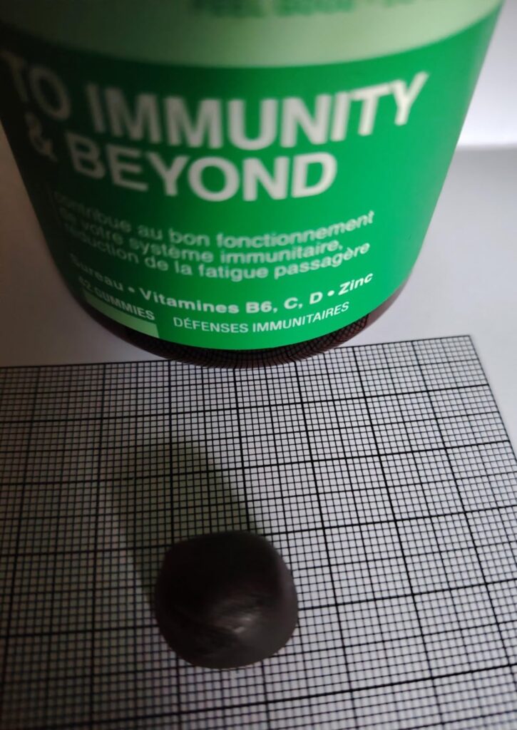 Vue d'une pastille sur une feuille quadrillée et une partie du flacon, axée sur la taille de la pastille
