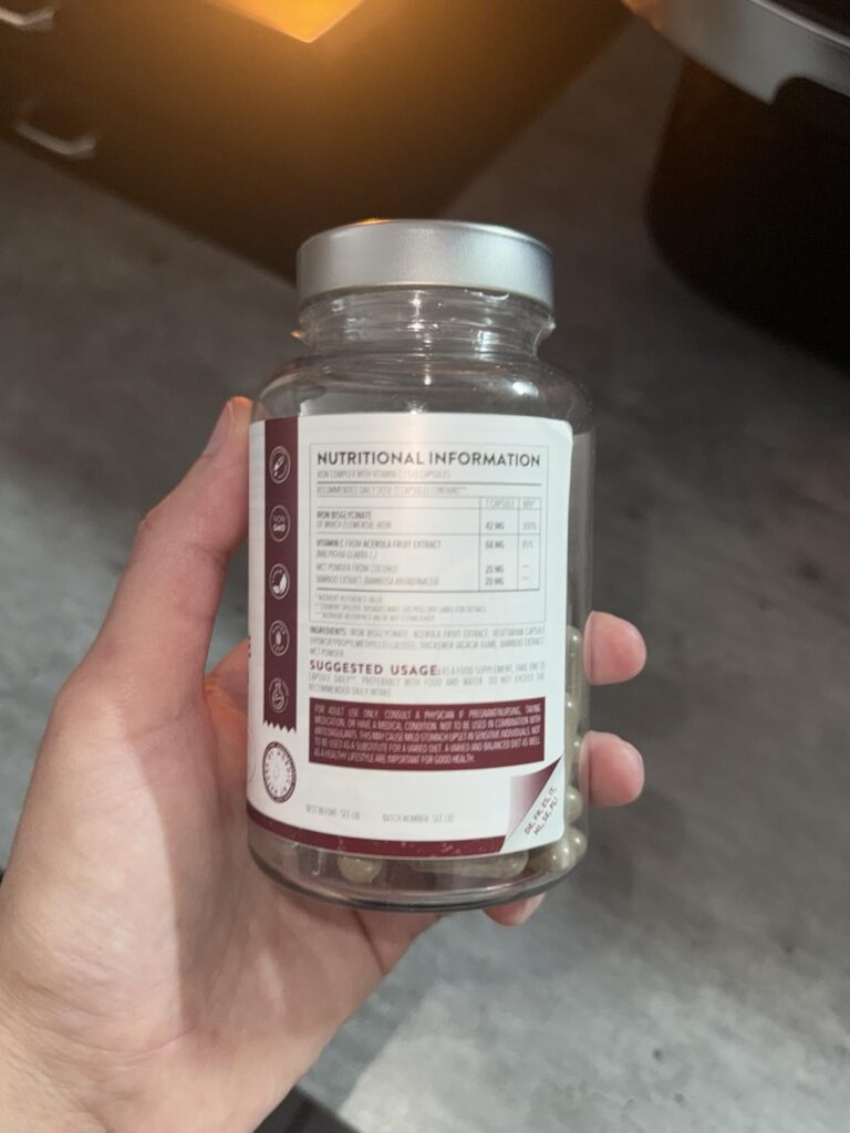 Bouteille de compléments alimentaires, marque Naturelo, tenue dans une main, vue de dos montrant l'étiquette nutritionnelle.