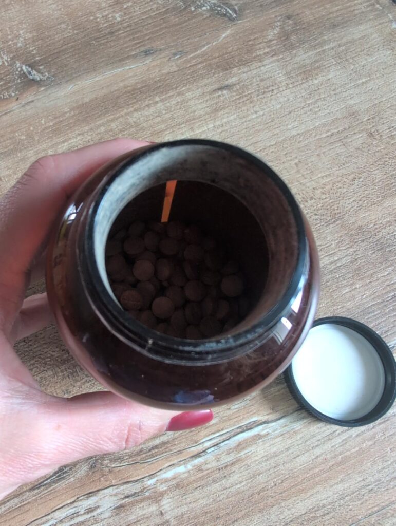 Gros plan sur l'intérieur du pot de gélules, vue plongeante sur les gélules, le bouchon est posé à côté.