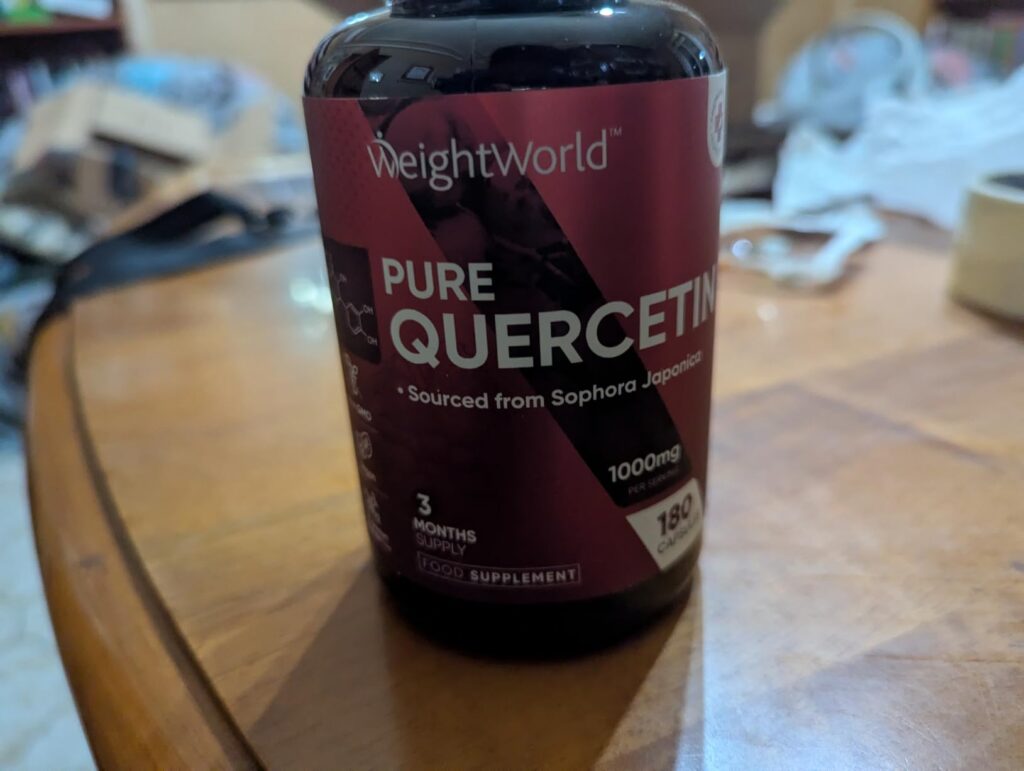 Bouteille de compléments alimentaires WeightWorld Pure Quercetin posée sur une table en bois, avec un arrière-plan flou d'int...