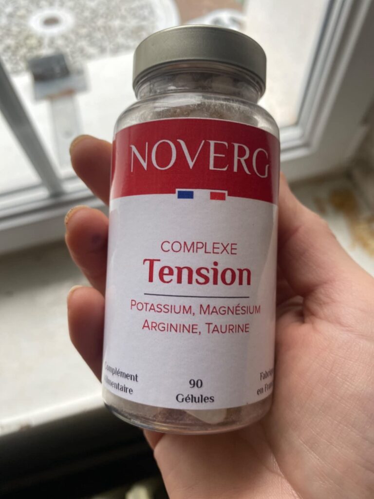 Bouteille de compléments alimentaires tenue à la main, en intérieur, angle de vue différent de l'image précédente