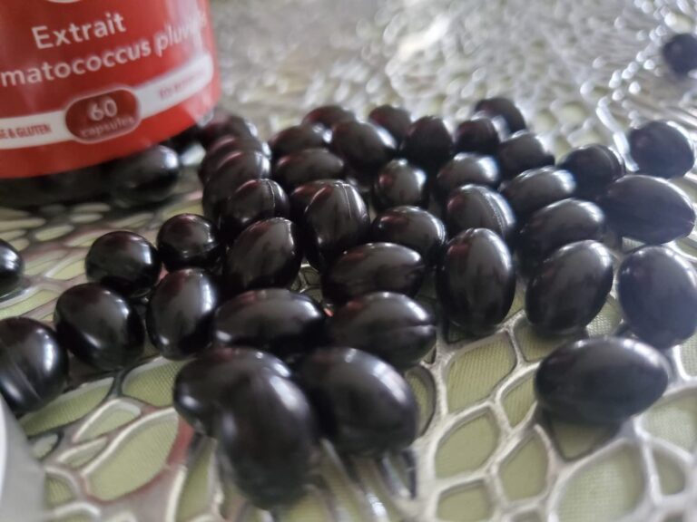 Plusieurs gélules noires sur une surface claire, avec le flacon en arrière-plan.