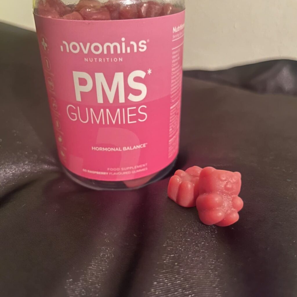 Le pot de gummies PMS et deux bonbons gélifiés en forme d'oursons sur un tissu gris.