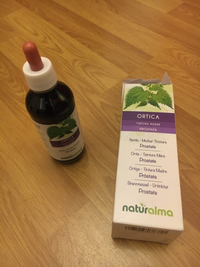 Le produit et son emballage posés sur un plancher en bois, le flacon est au premier plan à gauche et la boîte en carton est à...