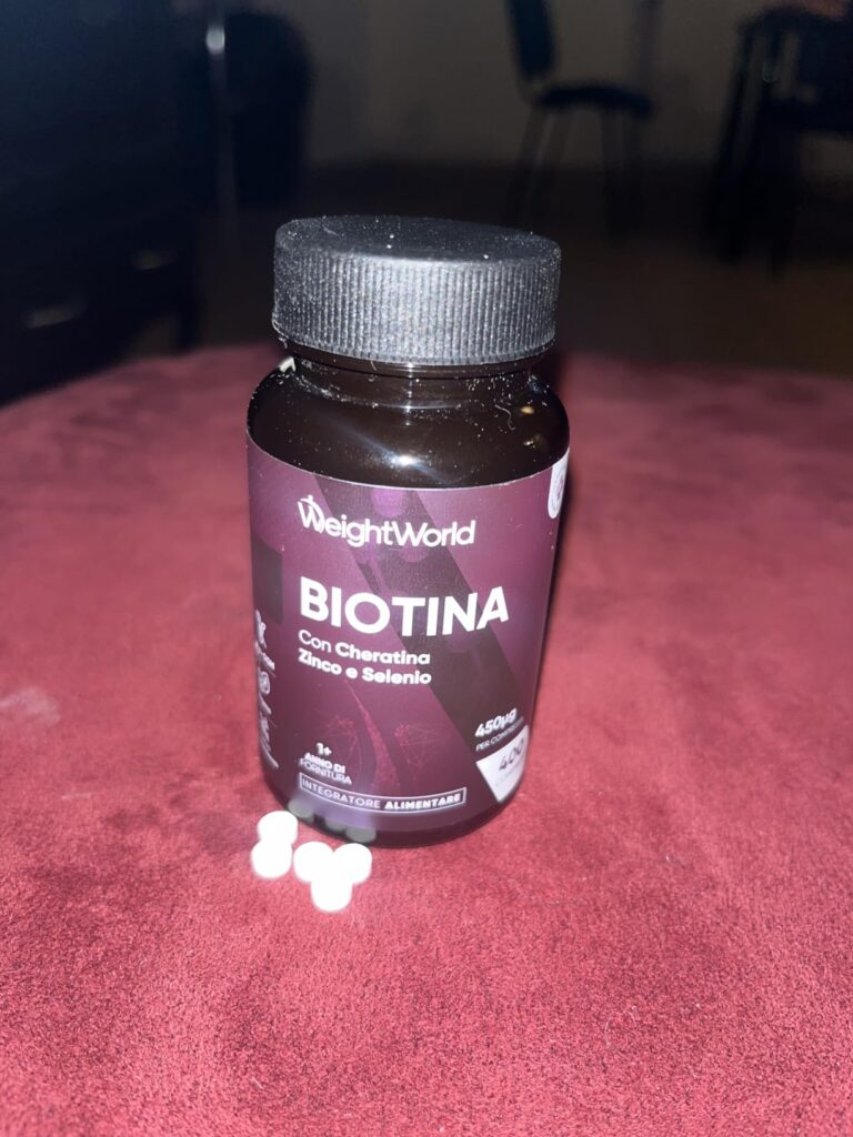 Le flacon de "Biotina" avec quelques comprimés blancs étalés sur une surface rouge. La photo est légèrement floue en arrière-...