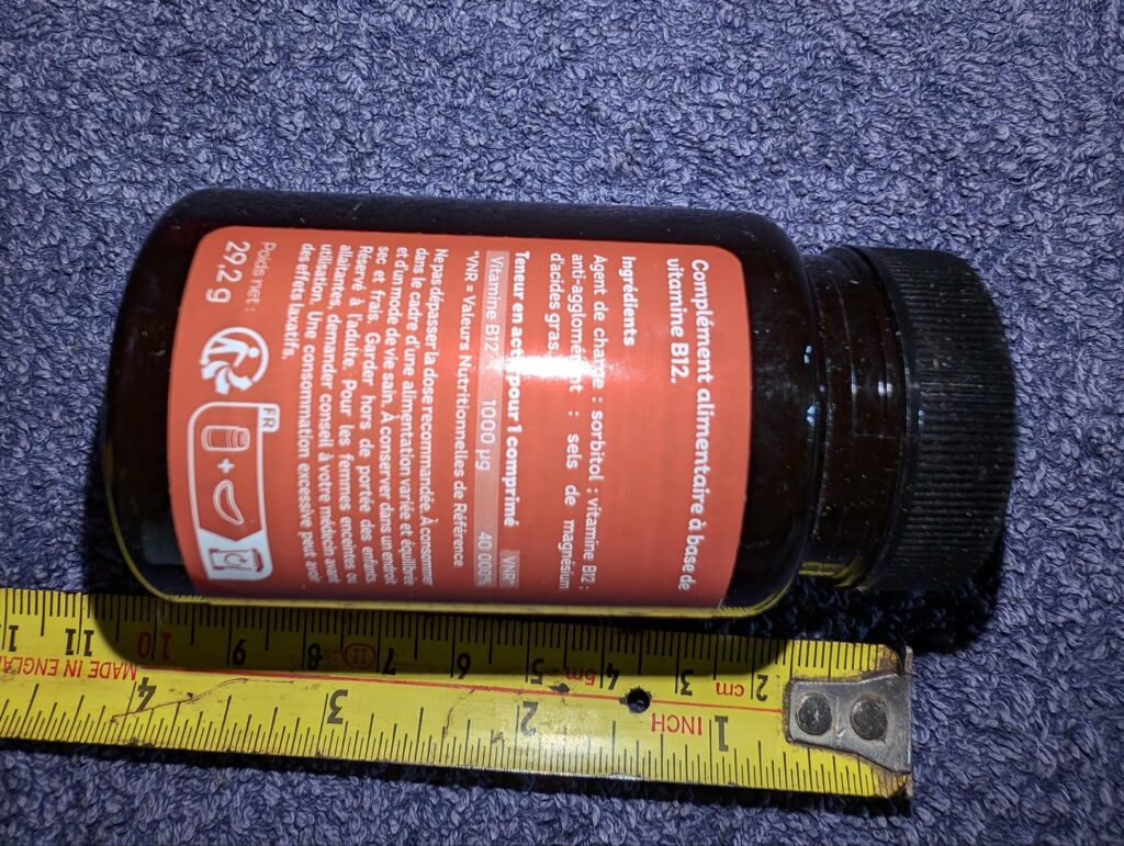 Flacon de vitamine B12 posé à côté d'un mètre-ruban, vue latérale, sur le côté avec l'étiquette.