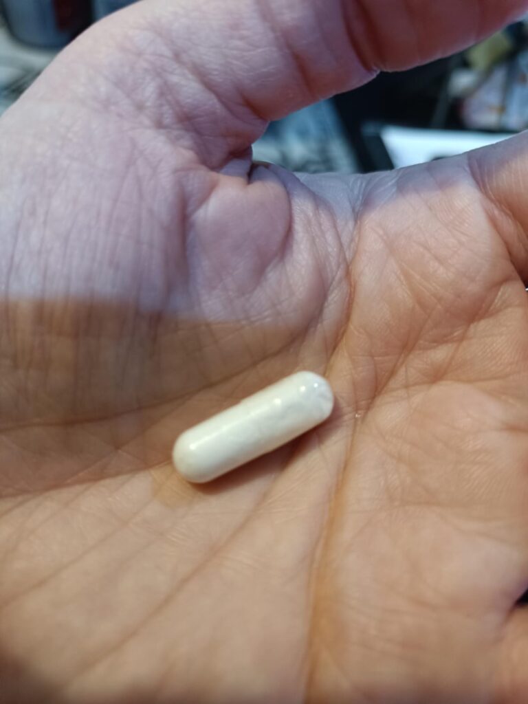 Une capsule blanche allongée de Taurine dans la paume d'une main.