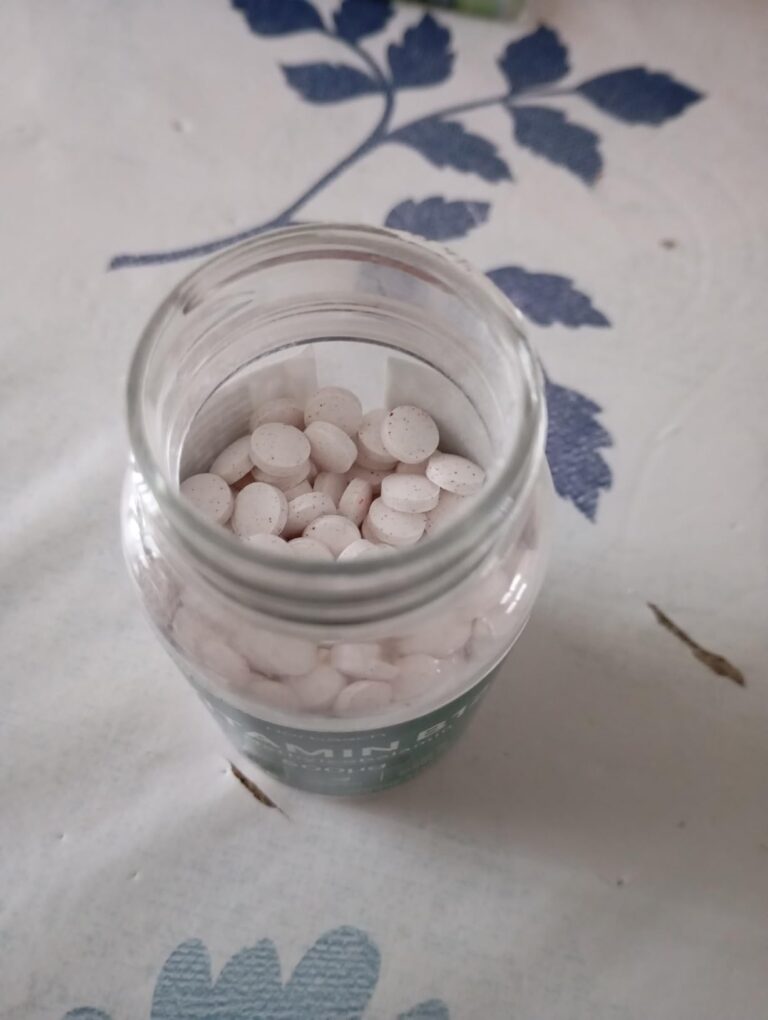 Vue de dessus d'un pot en verre rempli de comprimés ronds et blancs, posé sur une nappe blanche et bleue.