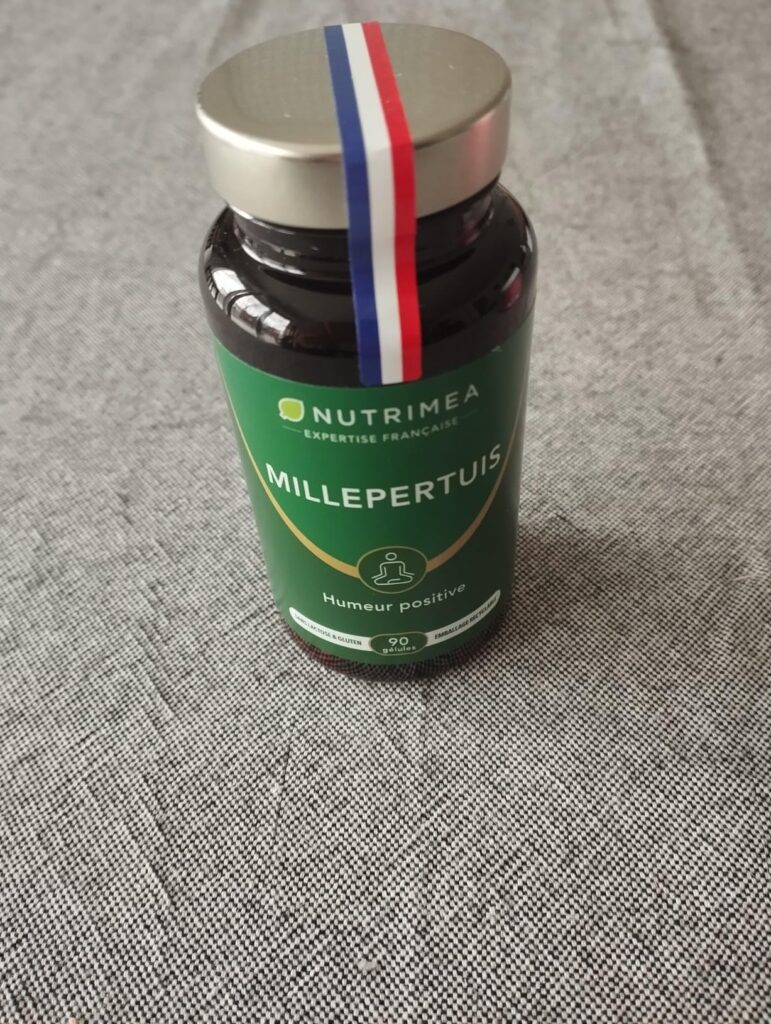 Flacon de Millepertuis Nutrimea posé sur un tissu gris, avec un ruban bleu-blanc-rouge sur le couvercle.