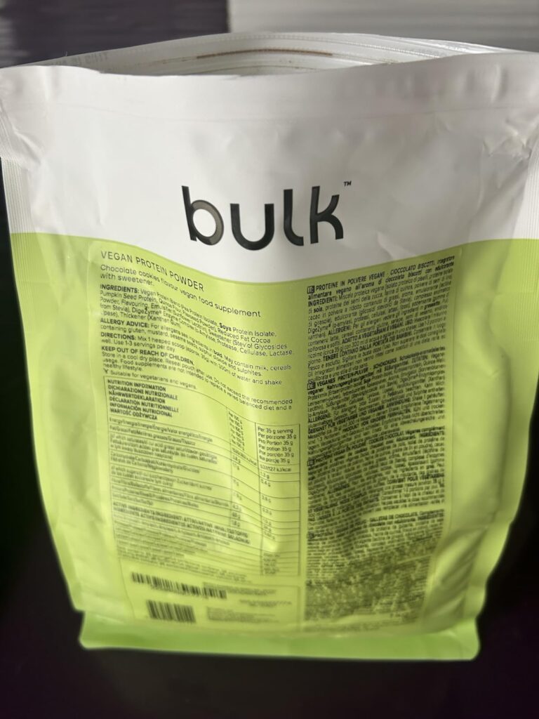 Vue de dos du sachet de poudre protéinée Bulk, posé sur une surface sombre. On peut lire la liste des ingrédients et le table...